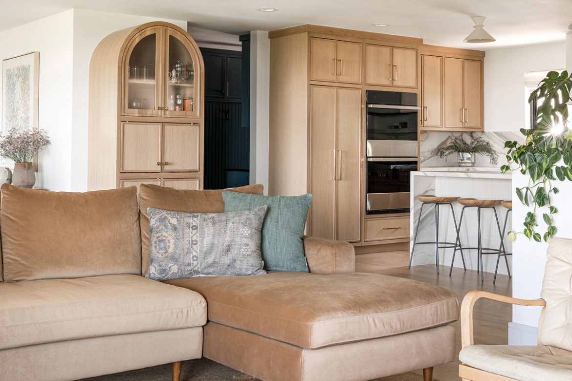 Open-concept living room and kitchen with wood cabinetry, marble accents, and a tan sectional.